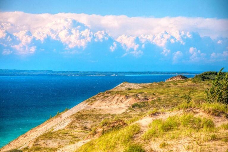 Grassy sand dune bluff above turquoise Lake Michigan at Sleeping Bear Dunes National Lakeshore, with an island and lighthouse in the distance