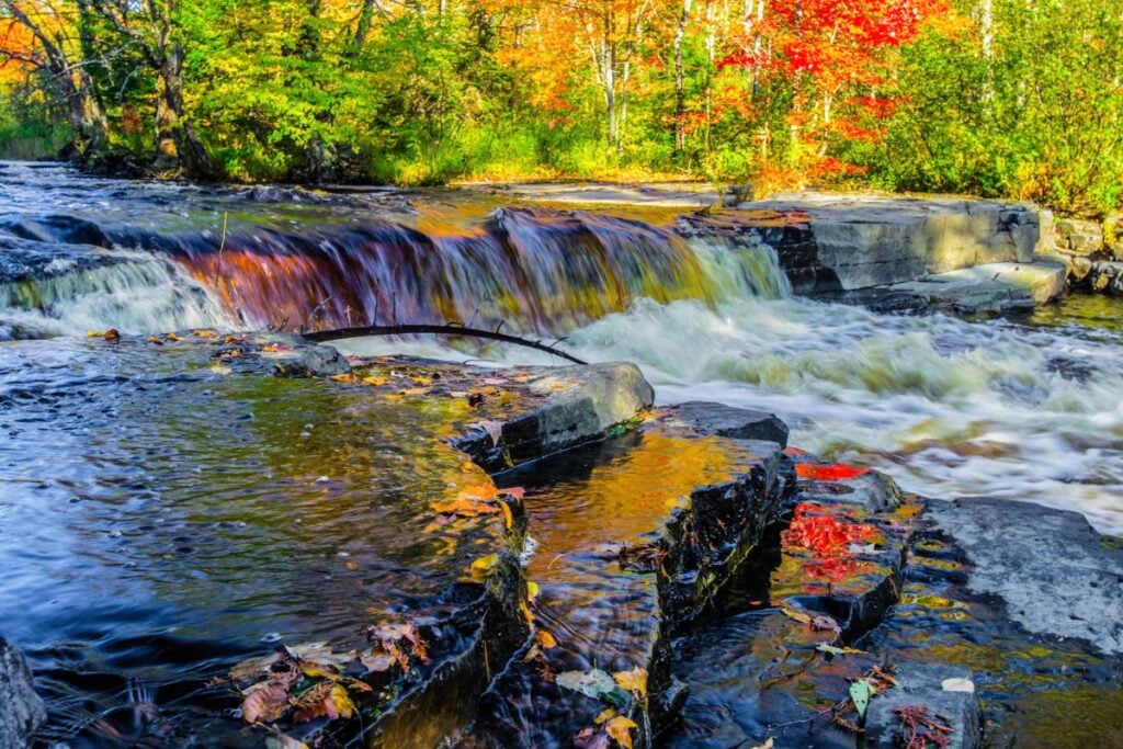 Sturgeon River cascading over dark rock ledges at Canyon Falls in Baraga County, Michigan, with red and gold fall leaves