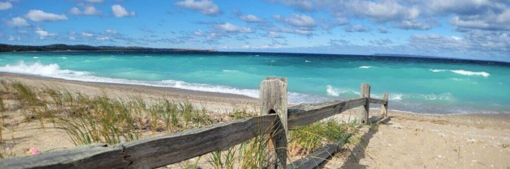 michigan beach with blue waterm white sand and fence