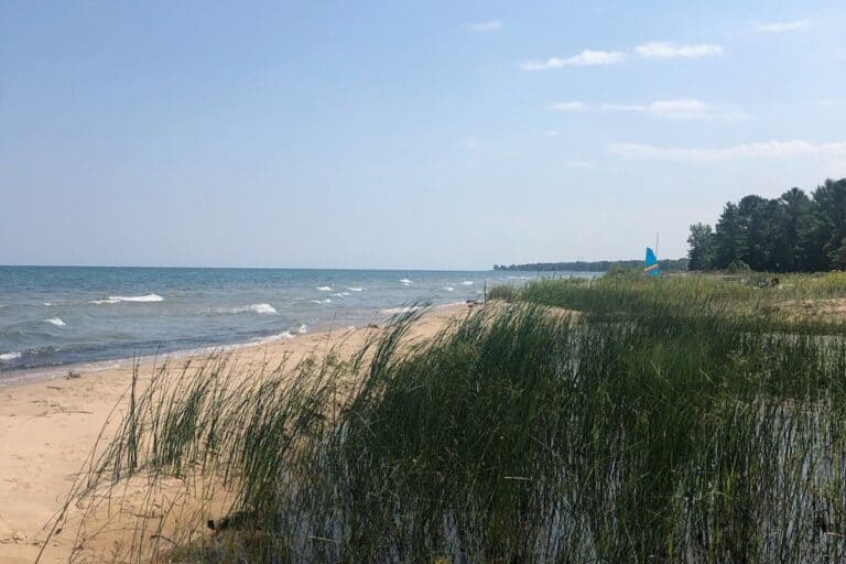 Lake Huron sandy beach with dunes and sailboat along Michigan shoreline