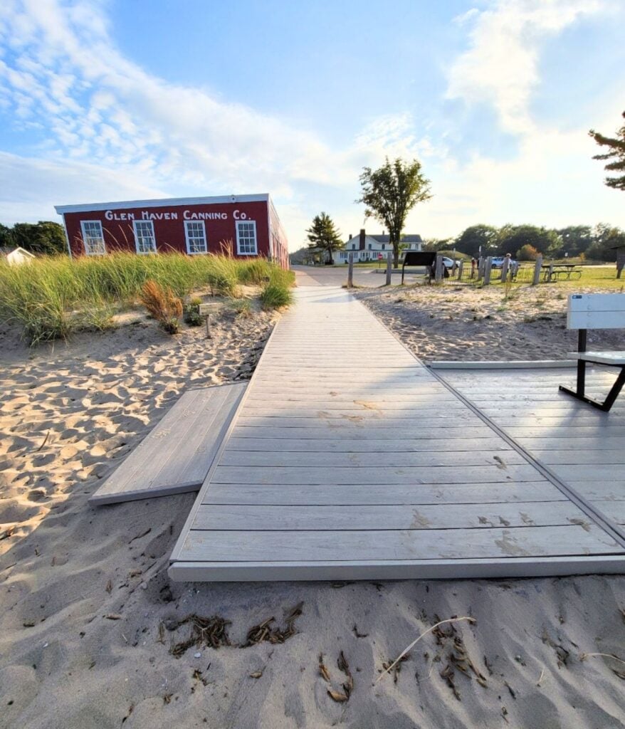 Accessible hard-surface boardwalk leading to Glen Haven Beach with the Glen Haven Canning Co. building behind