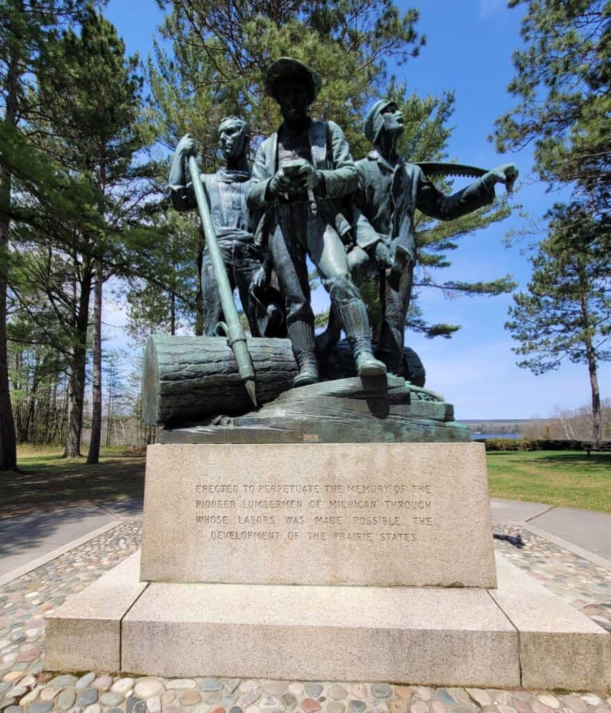 14-foot bronze Lumberman's Monument statue with inscription honoring Michigan's pioneer lumbermen on a bluff above the AuSable River in Oscoda, Michigan