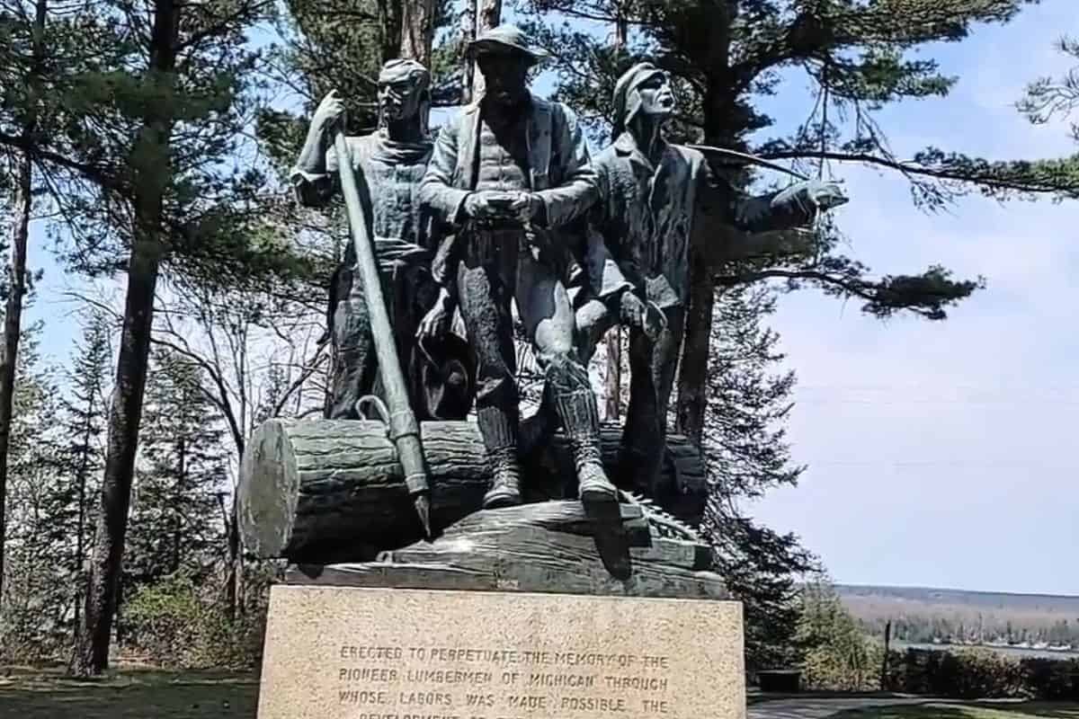 Close-up of the three bronze figures at Lumberman's Monument — a river rat, sawyer, and timber cruiser — in Oscoda, Michigan