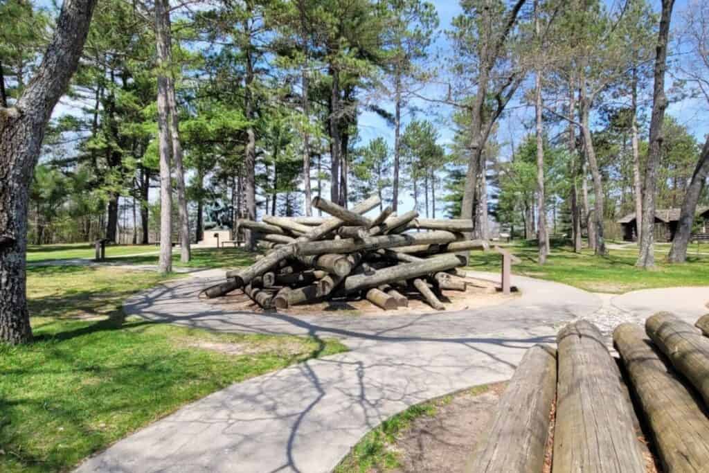 Stacked logs display and visitor center buildings, including the gift shop, at Lumberman's Monument in Oscoda, Michigan