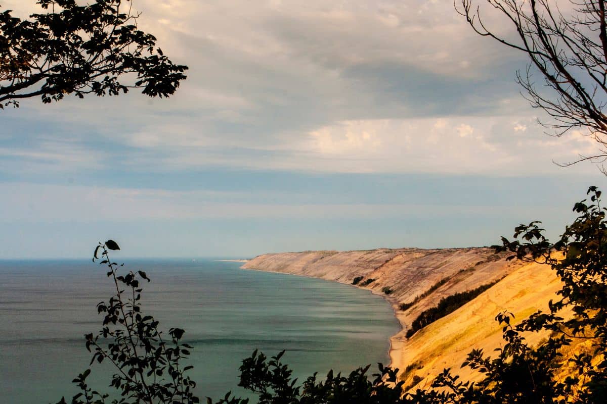 Sleeping Bear Dunes bluff face above Lake Michigan shoreline framed by autumn tree branches at golden hour