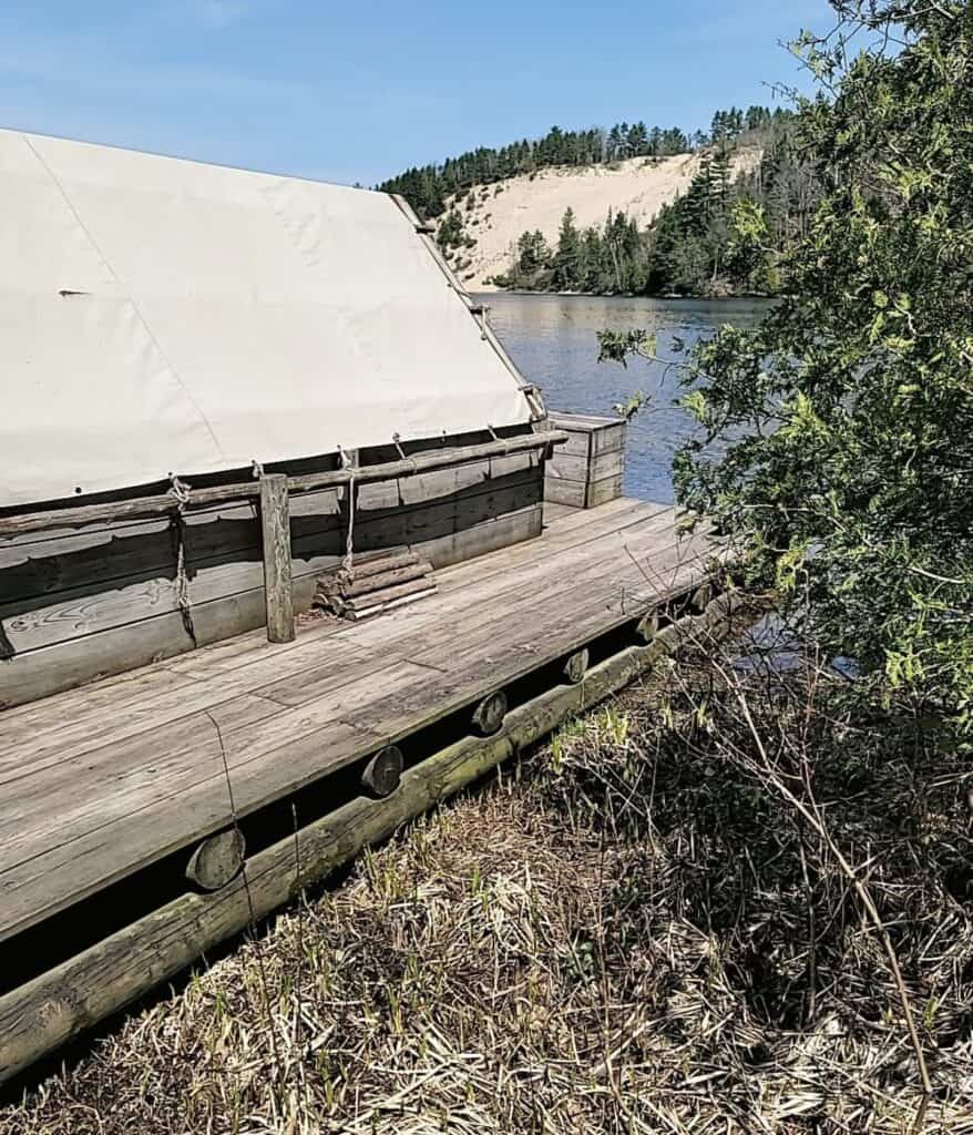 Side view of the canvas-topped wanigan cook shack on the AuSable River at Lumberman's Monument with the sand dune across the water in Oscoda, Michigan