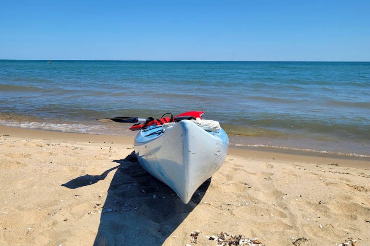 White kayak with paddle and red life vest pulled up on the sandy Lake Huron beach at Oscoda Michigan with calm water in the background