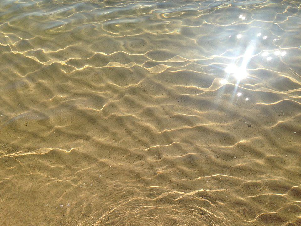 Sun sparkling on the crystal clear shallow water of Lake Huron at Oscoda Michigan with rippled sandy bottom visible