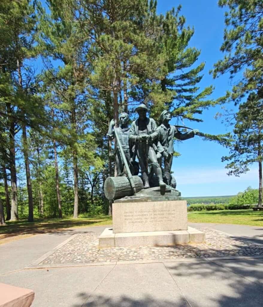 Bronze statue of three pioneer lumbermen at Lumberman's Monument near Oscoda Michigan with pine trees in the background