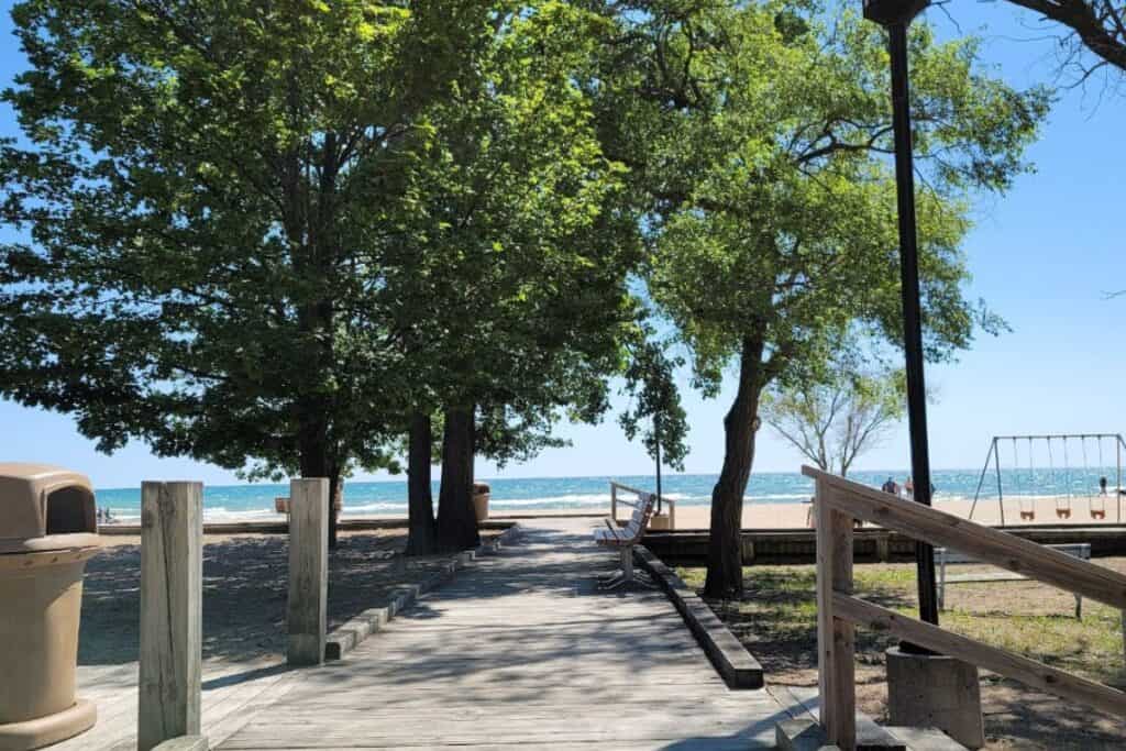 Wide ADA accessible wooden boardwalk leading through shade trees toward Lake Huron at Oscoda Beach Park Michigan