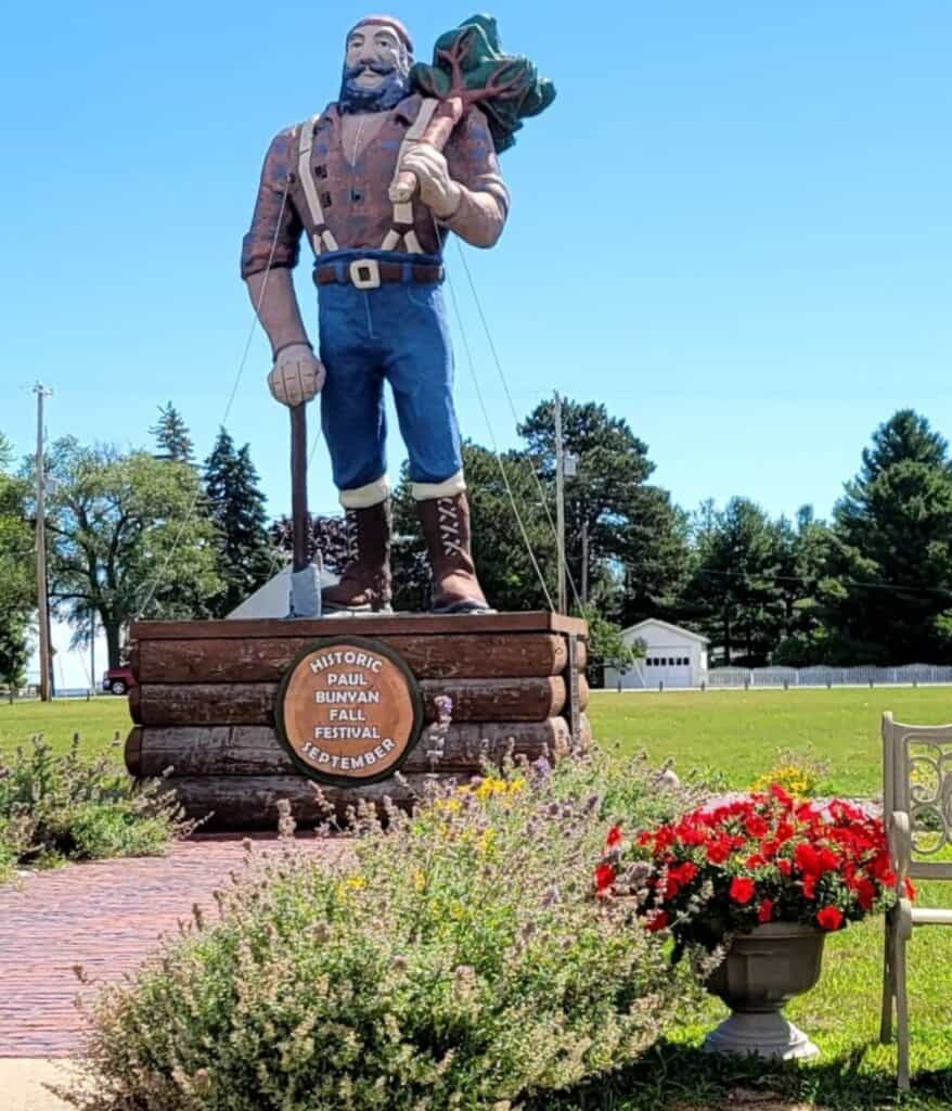 Historic Paul Bunyan Fall Festival statue in Oscoda Michigan with tree trunk pedestal and red flowers