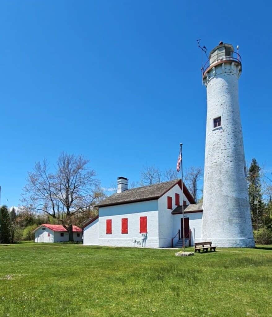 Sturgeon Point Lighthouse white tower with red-trimmed keeper's house and American flag in Harrisville Michigan