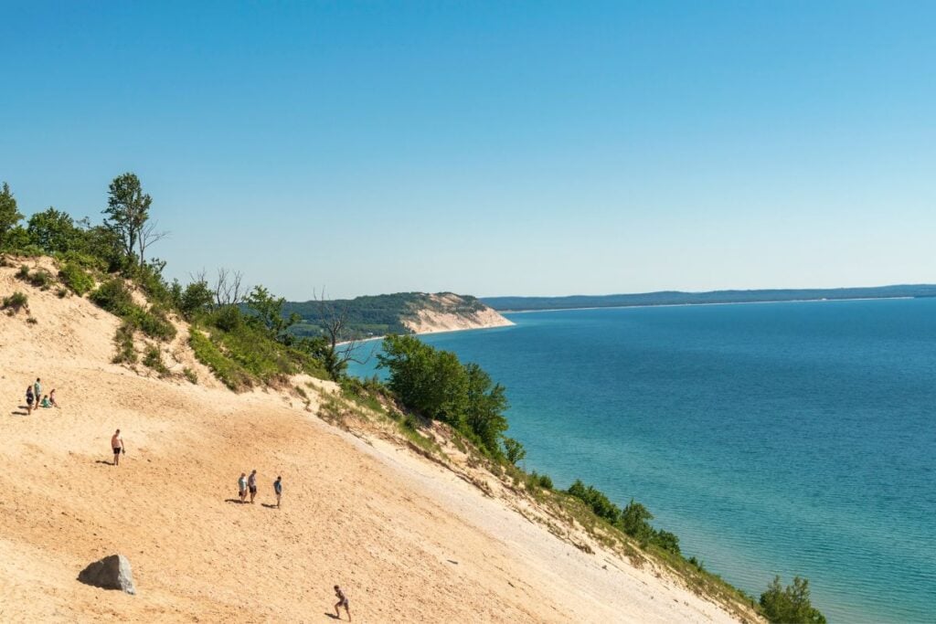 Visitors climbing the steep sand slope at Sleeping Bear Dunes National Lakeshore with Lake Michigan and the Empire bluffs in the distance
