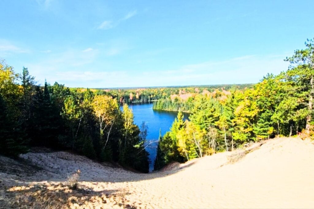 View from the sand bluff at Foote Pond Overlook looking down over blue water and fall color near Oscoda, Michigan
