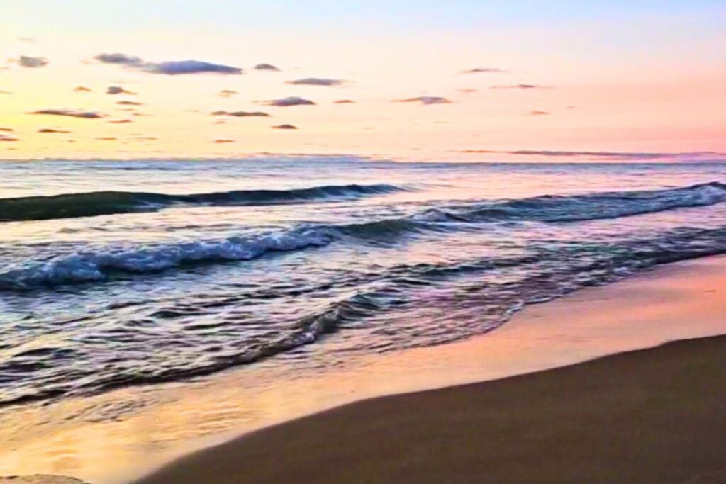 Pink and gold sunrise over Lake Huron with waves rolling onto the sand beach at Oscoda, Michigan in fall