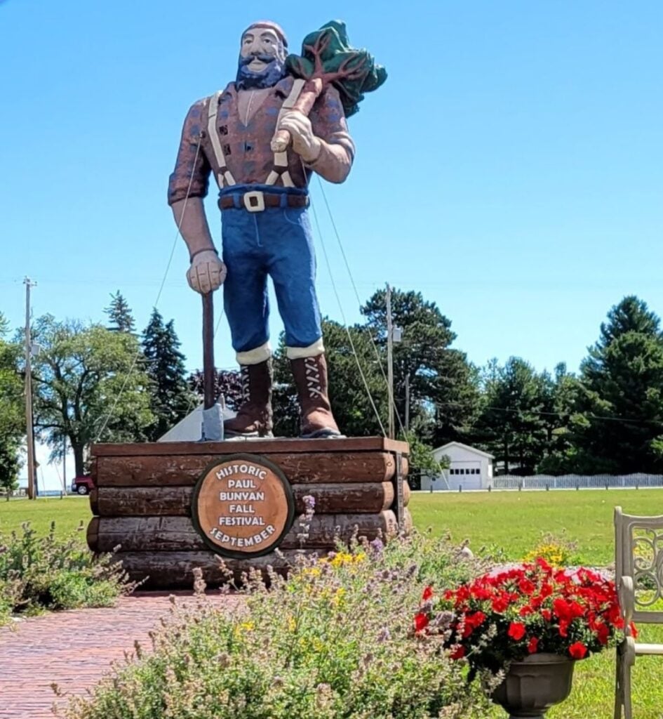 The Paul Bunyan statue at Furtaw Field in Oscoda, Michigan, standing on a log base with a sign for the Historic Paul Bunyan Fall Festival