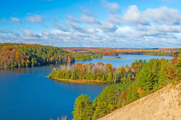 Blue AuSable River impoundment with forested islands in peak fall color, seen from a sand dune near Oscoda, Michigan