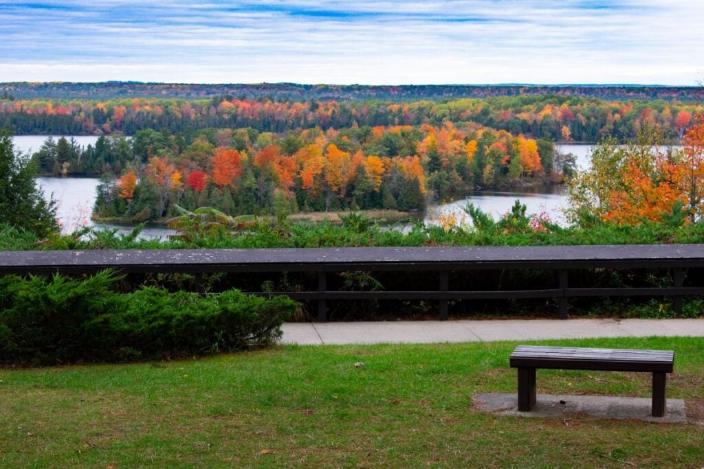 Paved overlook with a bench and railing above the AuSable River valley in peak fall color near Oscoda, Michigan